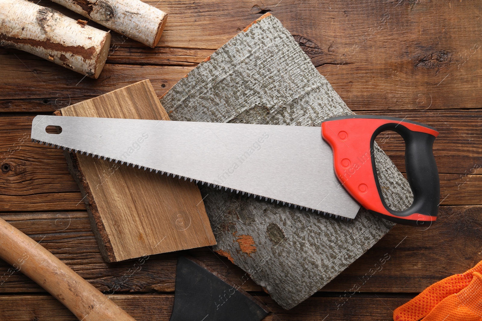 Photo of Saw with colorful handle, axe and logs on wooden background, flat lay