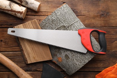 Photo of Saw with colorful handle, axe and logs on wooden background, flat lay