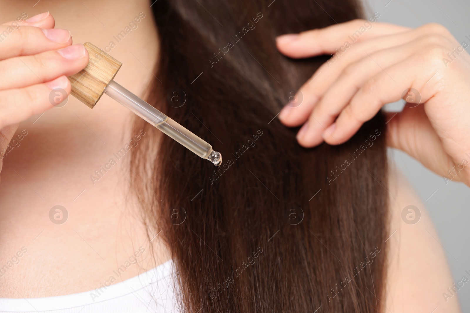 Photo of Woman applying essential oil onto hair on grey background, closeup