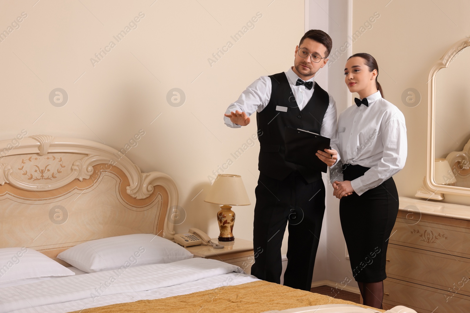 Photo of Young woman attending professional butler courses and teacher with clipboard in hotel room