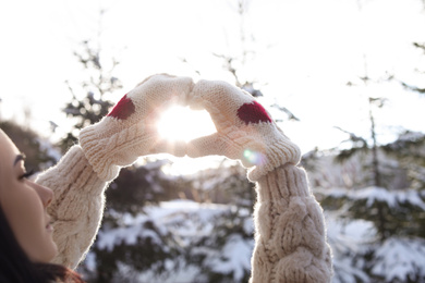 Young woman making heart with hands outdoors, closeup. Winter vacation