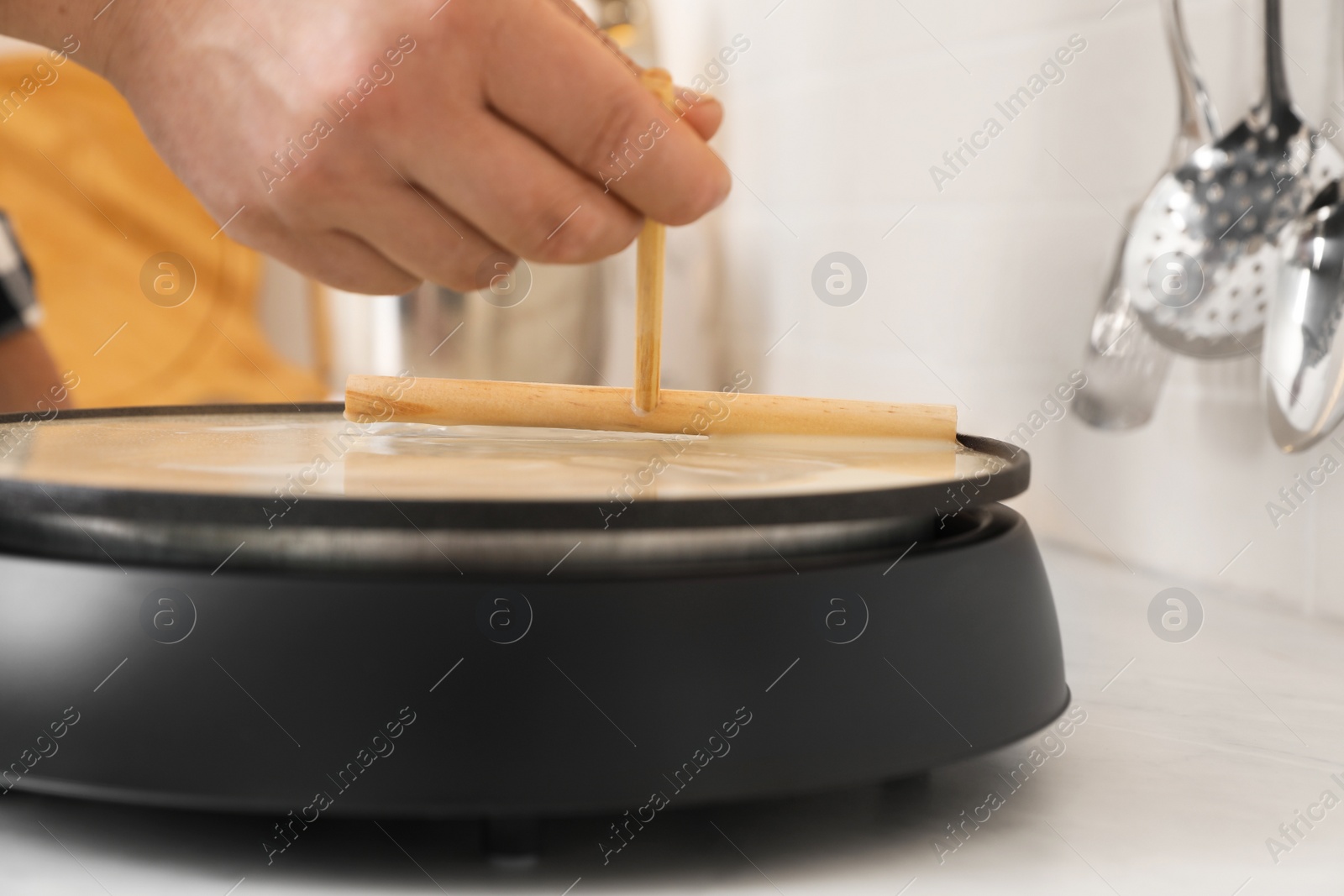 Photo of Man cooking delicious crepe on electric pancake maker in kitchen, closeup