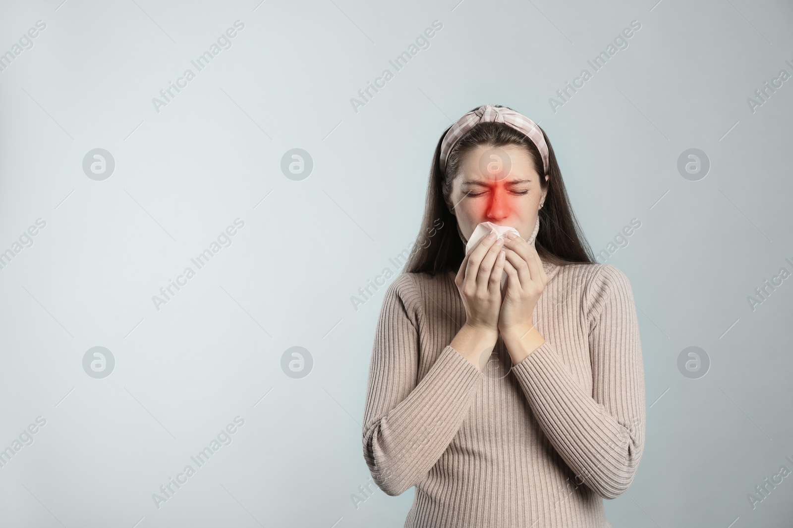 Image of Young woman with tissue suffering from runny nose on light background. Space for text