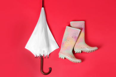 Photo of Beautiful white umbrella and colorful rubber boots on red background, flat lay