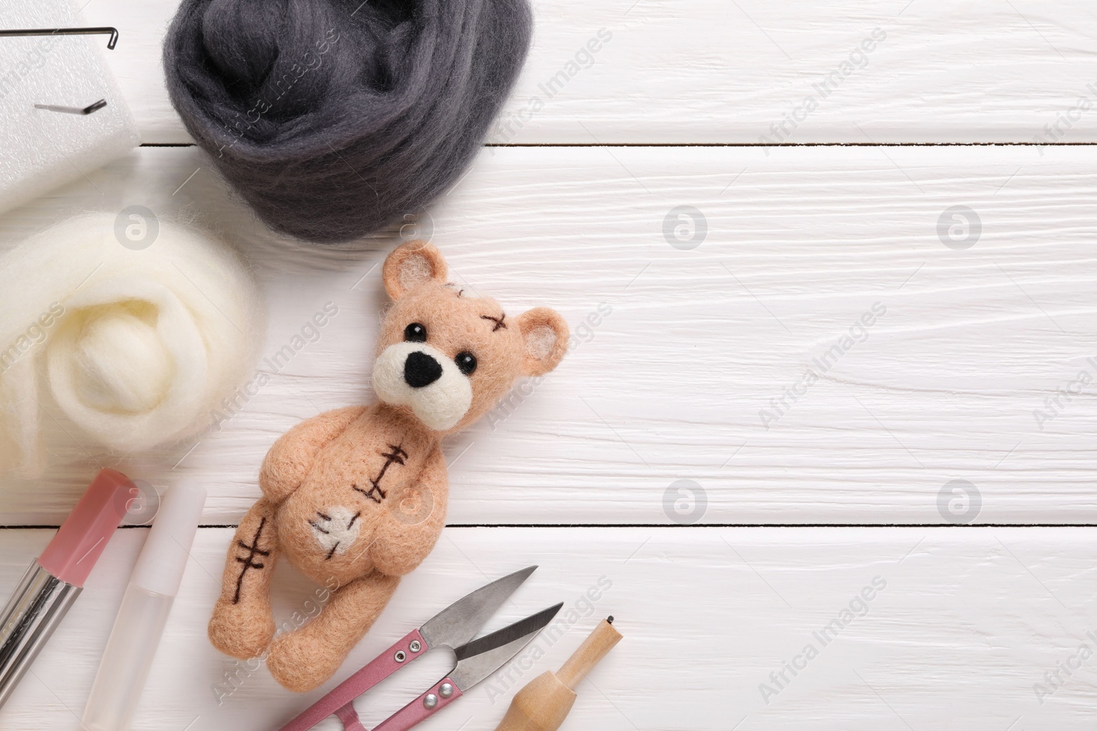 Photo of Felted bear, wool and tools on white wooden table, flat lay. Space for text