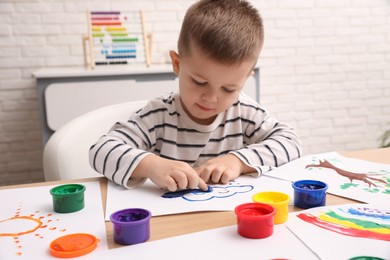 Little boy painting with finger at wooden table in room