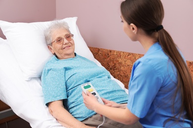 Nurse assisting senior woman lying on bed in hospital ward