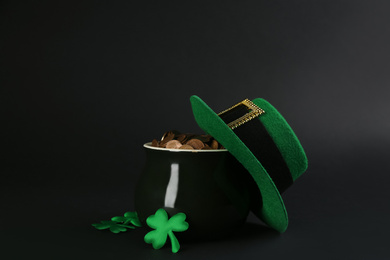 Photo of Pot of gold coins, hat and clover leaves on black background. St. Patrick's Day celebration