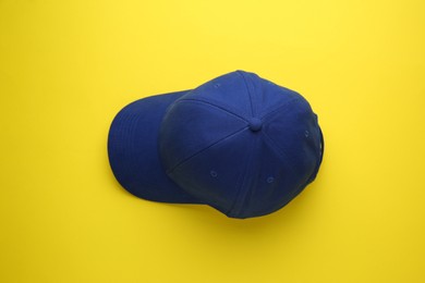 Photo of Stylish blue baseball cap on yellow background, top view