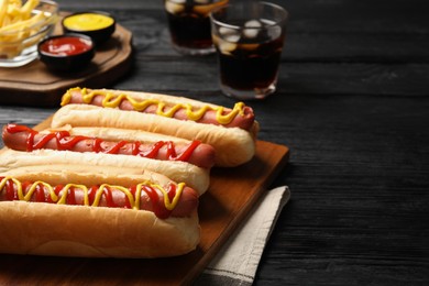 Delicious hot dogs with mustard and ketchup on black wooden table, closeup. Space for text