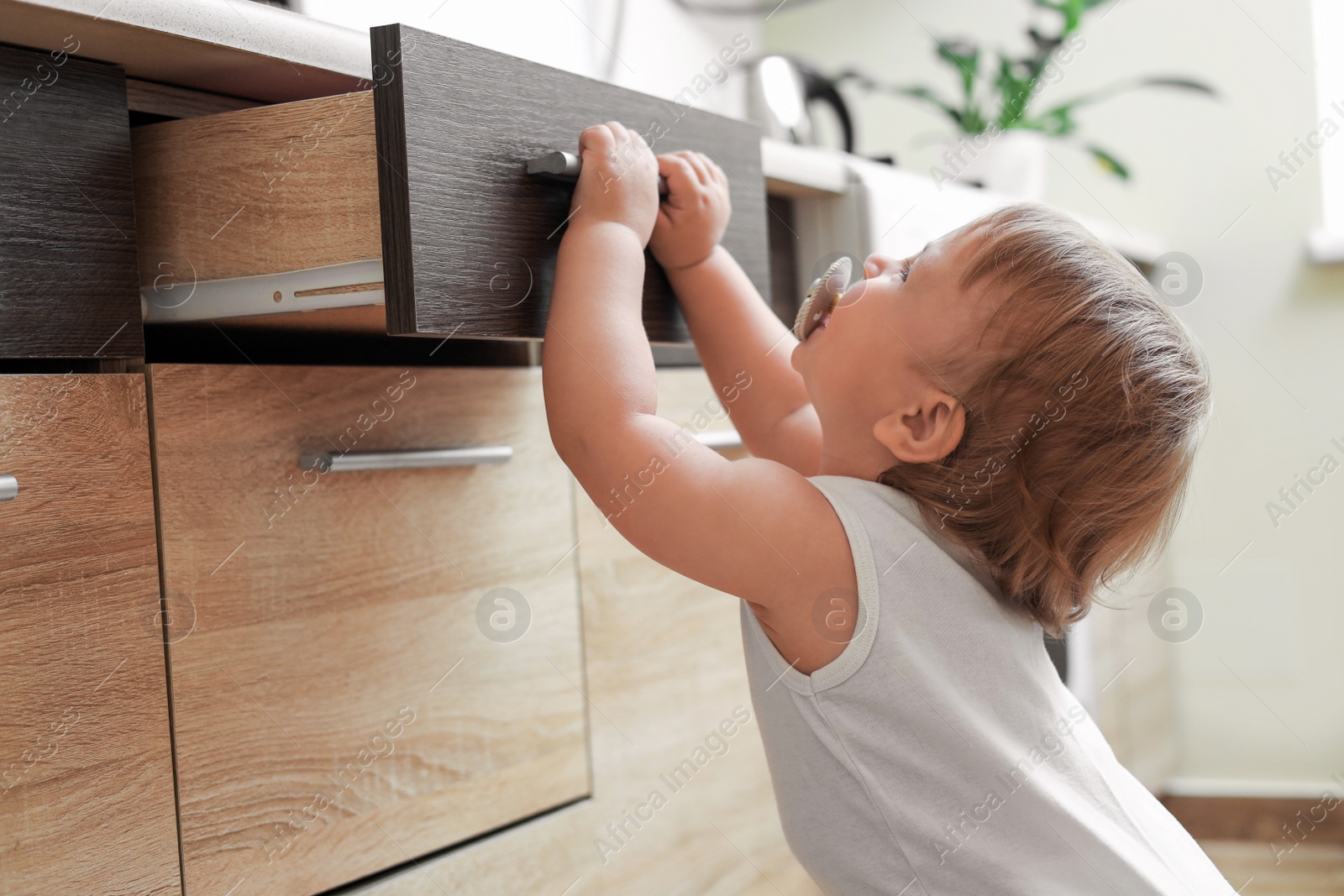 Photo of Little child exploring drawer indoors. Dangerous situation