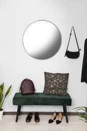 Hallway interior with black bench, shoes and round mirror on light wall