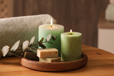 Photo of Spa composition. Burning candles, soap, towel and eucalyptus branch on wooden table