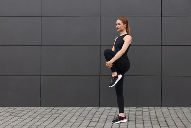 Beautiful woman in gym clothes doing exercises near dark grey wall on street, space for text
