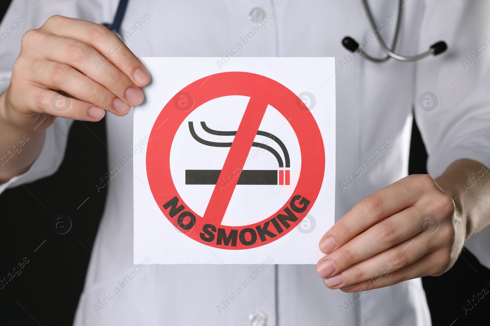 Photo of Doctor holding card with no smoking sign on black background, closeup