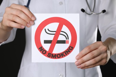 Doctor holding card with no smoking sign on black background, closeup