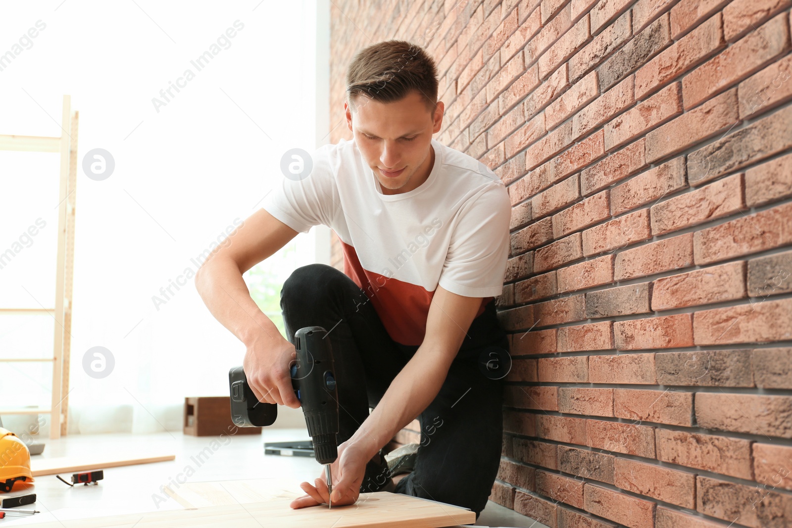 Photo of Young man working with electric screwdriver near brick wall