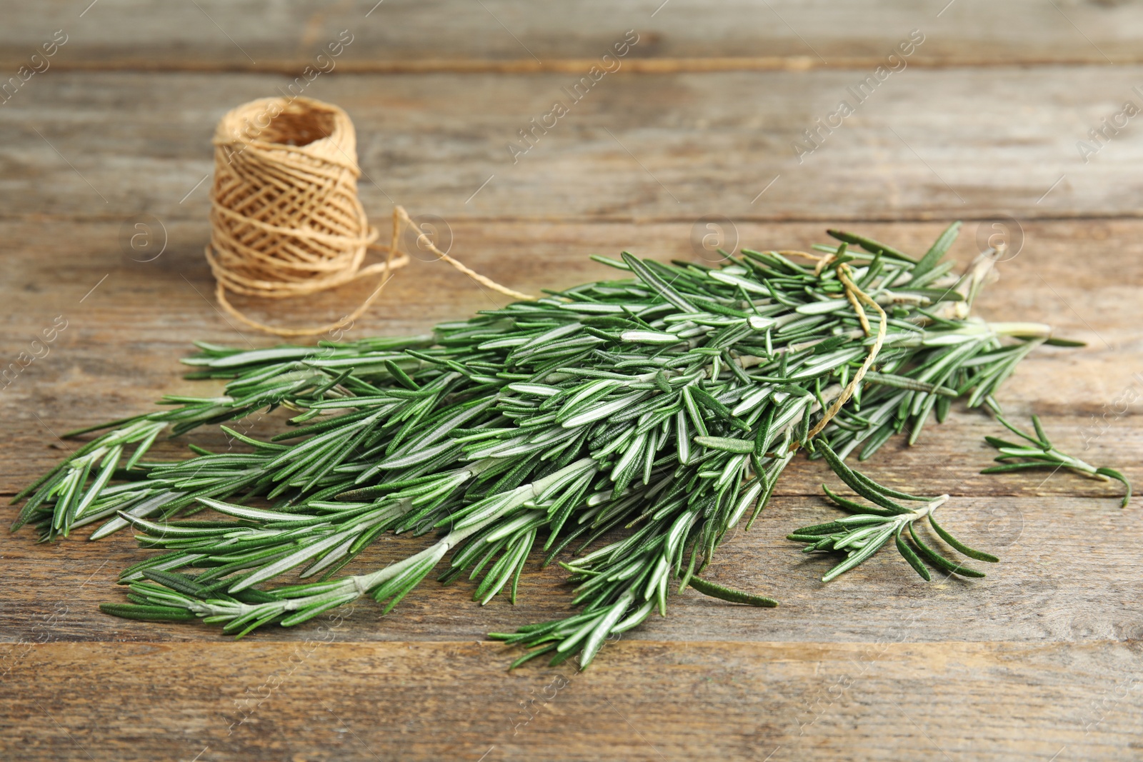 Photo of Fresh rosemary branches and twine on wooden table