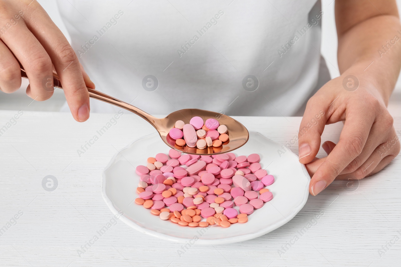 Photo of Woman sitting at table with spoon and plate of weight loss pills, closeup