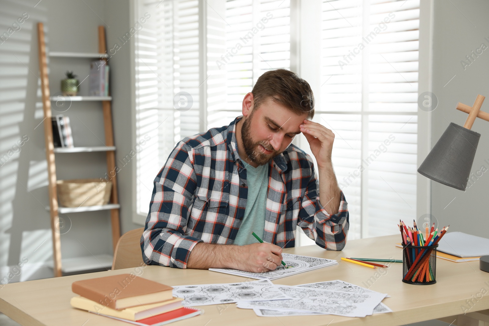 Photo of Young man coloring antistress picture at table indoors