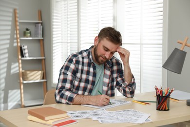 Young man coloring antistress picture at table indoors