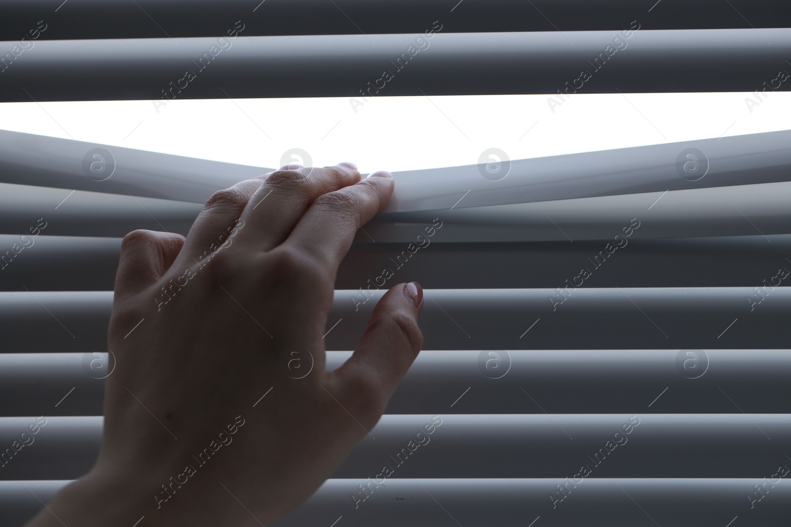 Photo of Woman separating slats of white blinds indoors, closeup