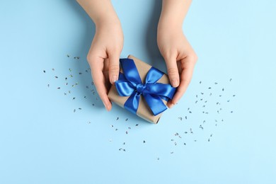 Photo of Woman with gift box and confetti on light blue background, top view