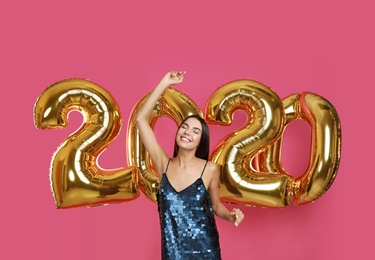 Happy young woman near golden 2020 balloons on pink background. New Year celebration