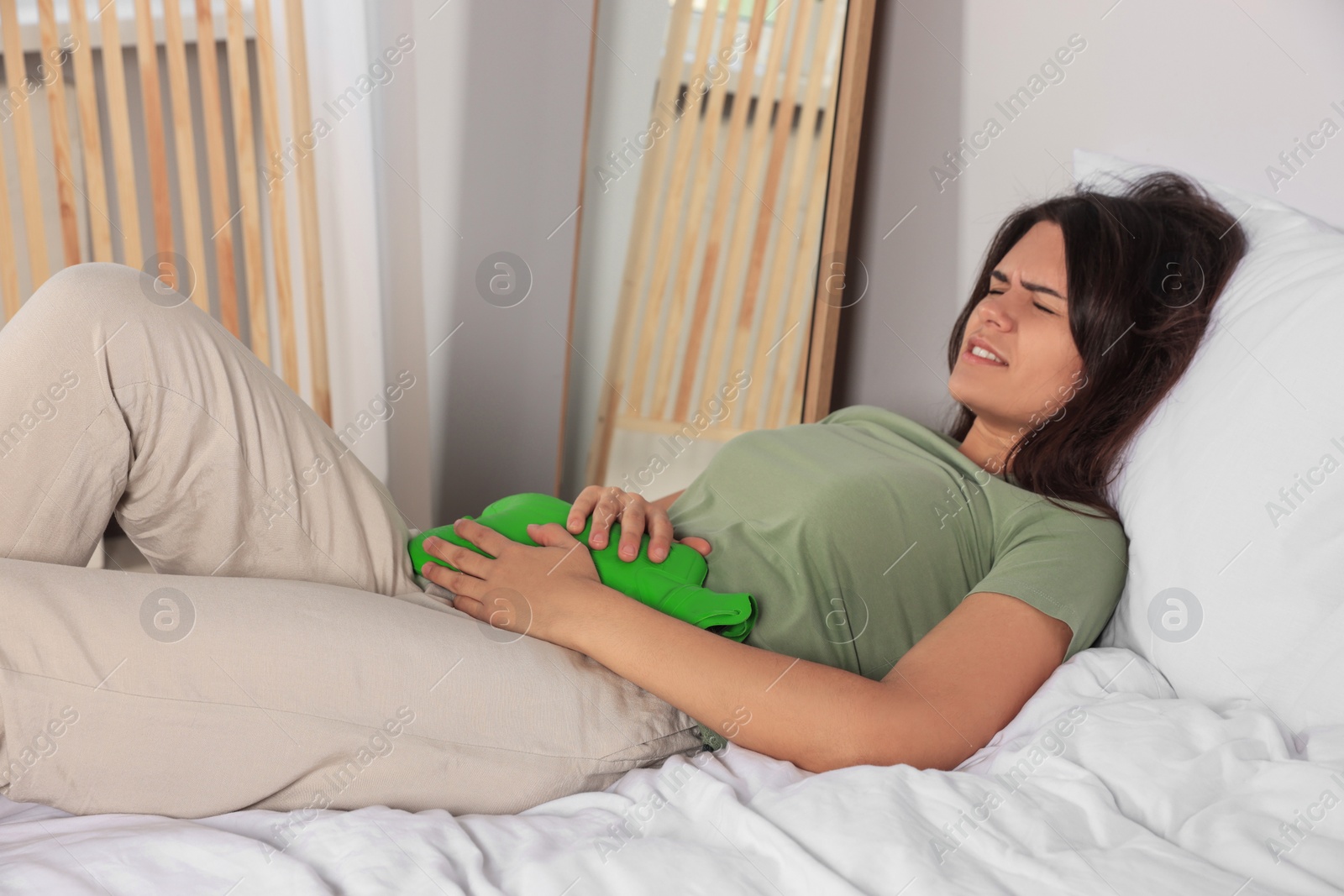 Photo of Young woman using hot water bottle to relieve cystitis pain on bed at home