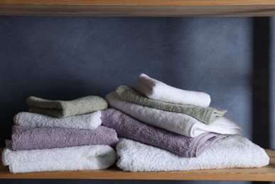 Photo of Stacked soft towels on wooden shelf indoors