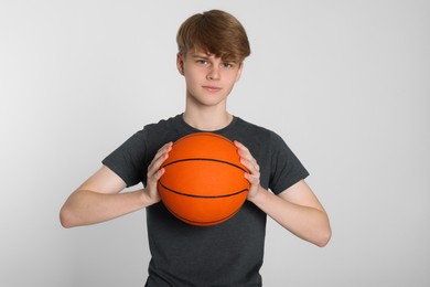 Teenage boy with basketball ball on light grey background