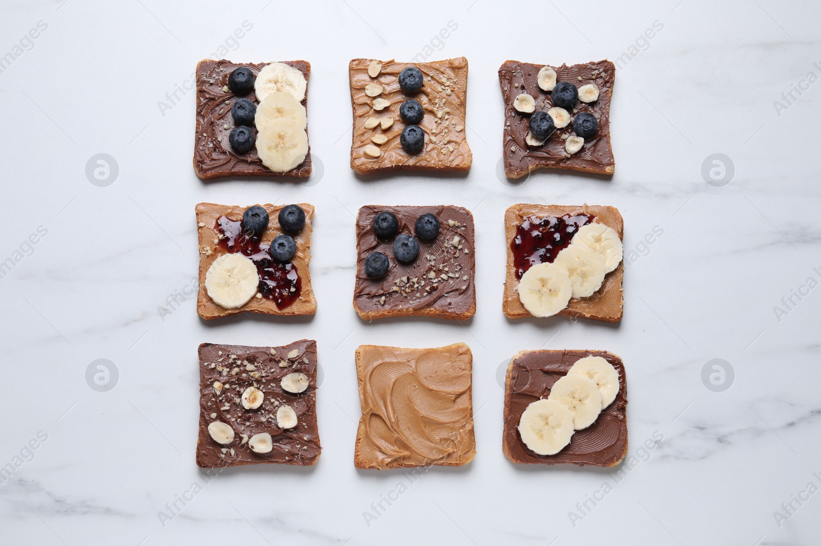 Photo of Different tasty toasts with nut butter and products on white marble table, flat lay