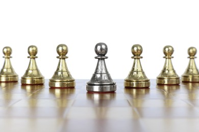 Photo of Silver pawn among golden ones on wooden chess board against white background