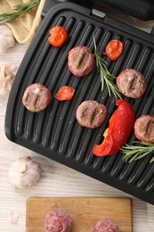 Photo of Electric grill with vegetables, meat balls and rosemary on wooden table, flat lay