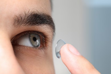 Photo of Closeup view of young man putting in contact lens on blurred background