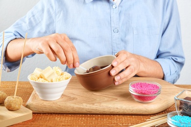 Photo of Young woman putting cake pop into chocolate frosting at wooden table, closeup