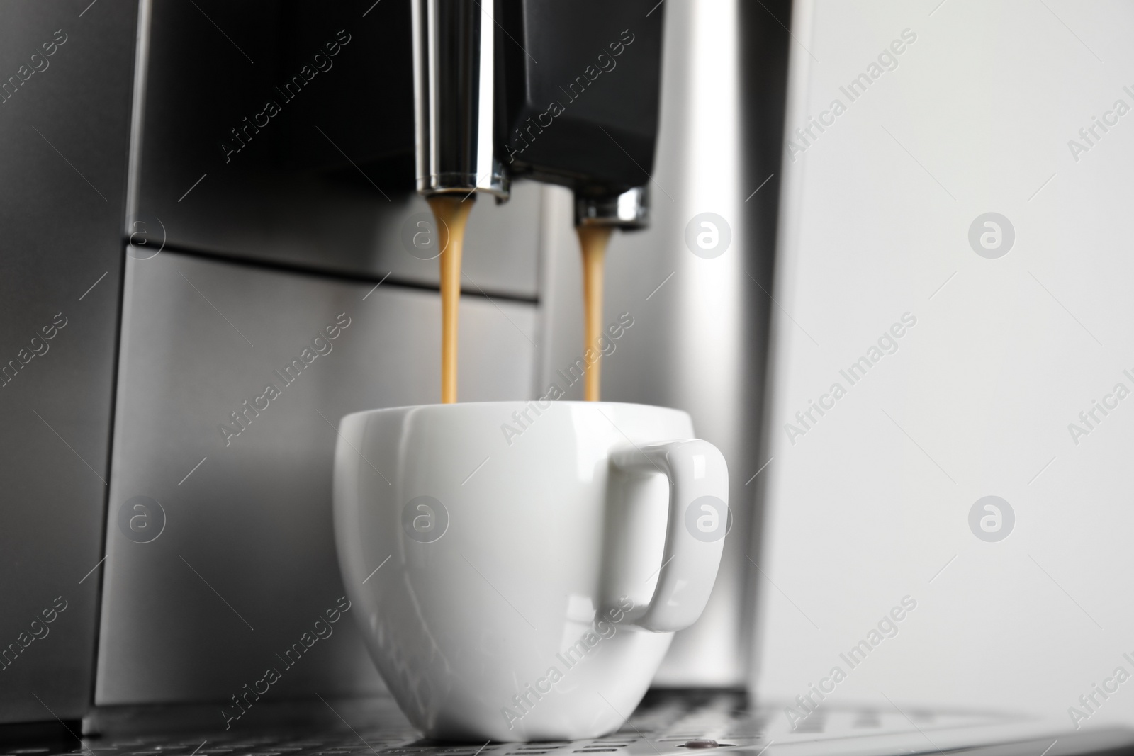 Photo of Espresso machine pouring coffee into cup against light background, closeup