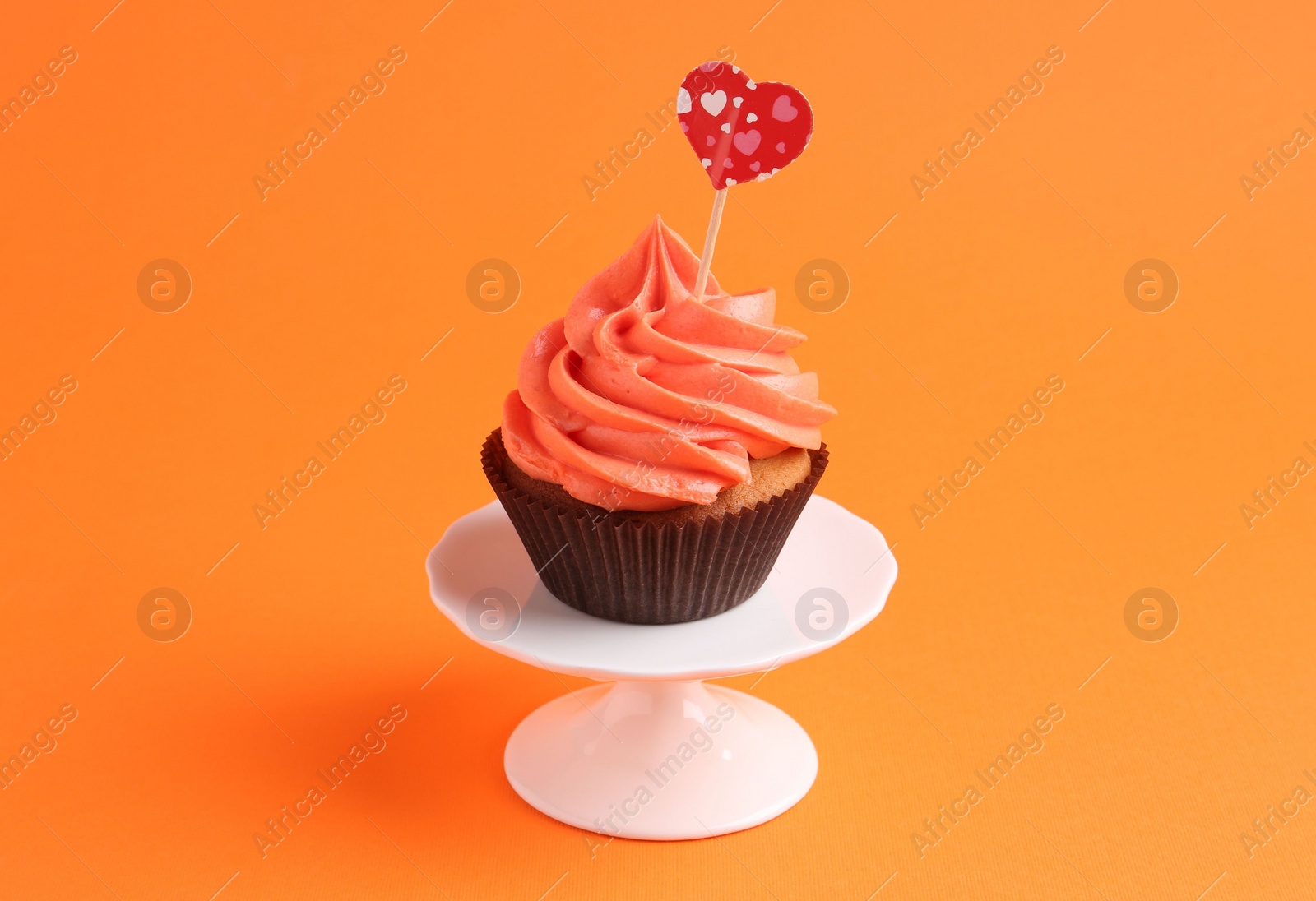 Photo of Delicious cupcake with bright cream and heart topper on orange background