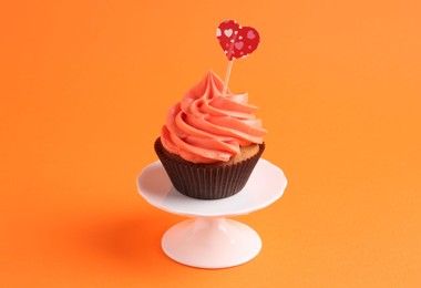 Photo of Delicious cupcake with bright cream and heart topper on orange background