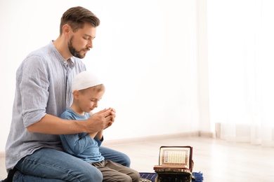 Photo of Muslim man and his son praying together indoors. Space for text