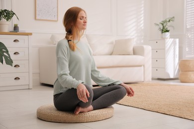 Woman meditating on wicker mat at home
