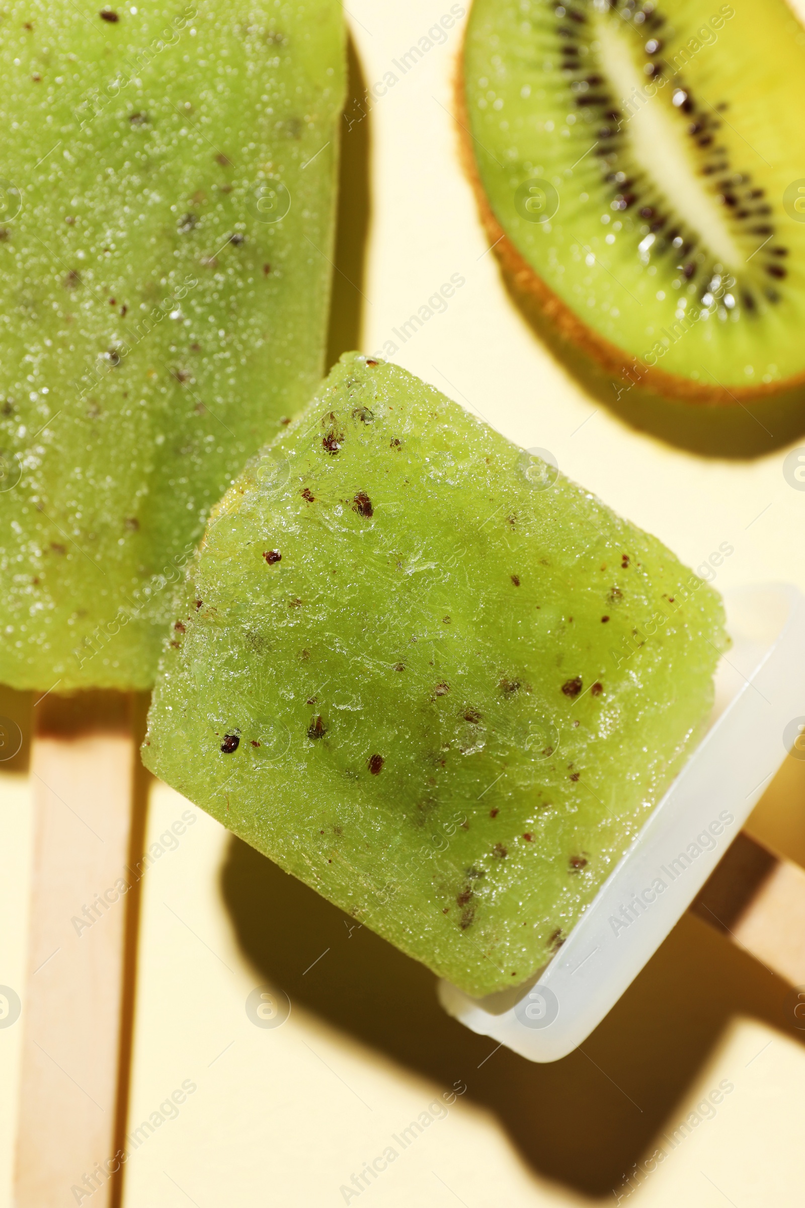 Photo of Tasty kiwi ice pops on pale light beige background. Fruit popsicle