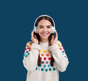 Young woman listening to music with headphones on dark blue background, space for text