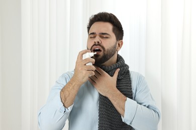 Photo of Young man with scarf using throat spray indoors