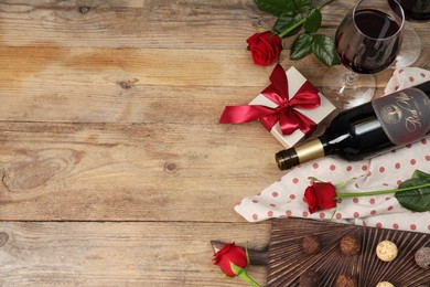 Photo of Red wine, chocolate truffles, gift box and roses on wooden table, flat lay. Space for text