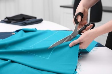 Seamstress cutting fabric at table in tailor workshop, closeup