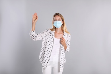 Photo of Woman in protective face mask showing hello gesture on grey background. Keeping social distance during coronavirus pandemic