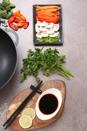 Photo of Wok, chopsticks and different products on grey textured table, flat lay