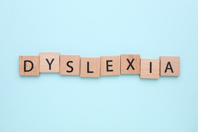 Wooden tiles with word Dyslexia on light blue background, flat lay