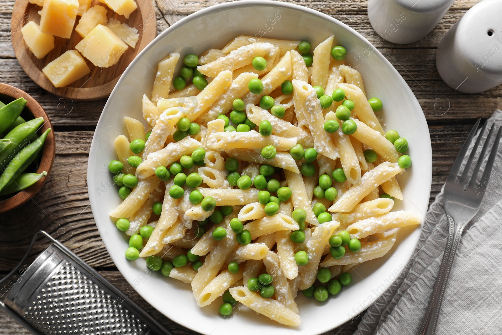 Photo of Delicious pasta with green peas, cheese, grater and fork on wooden table, top view